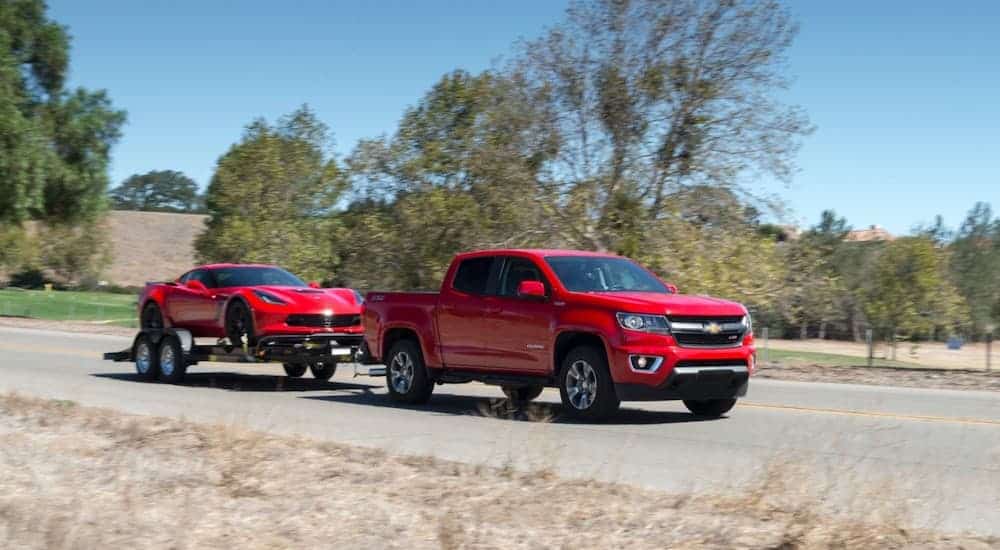A red 2017 Chevy Colorado is towing a red corvette down an empty road.