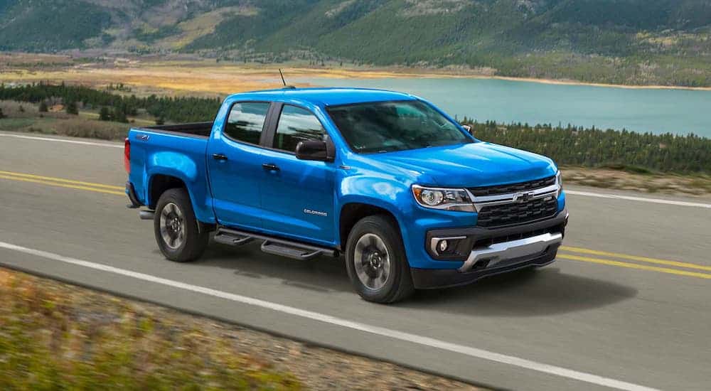 A bright blue 2021 Chevy Colorado is driving on a highway in front of a distant lake.