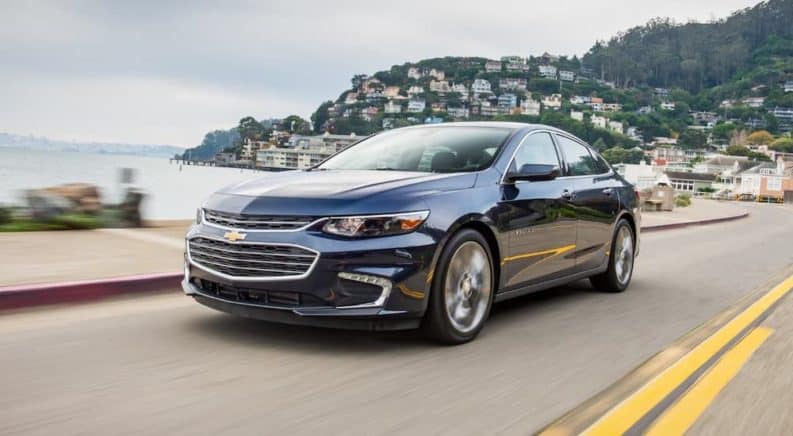 A blue 2021 Chevy Malibu is driving past a lake after leaving a Chevy dealership.