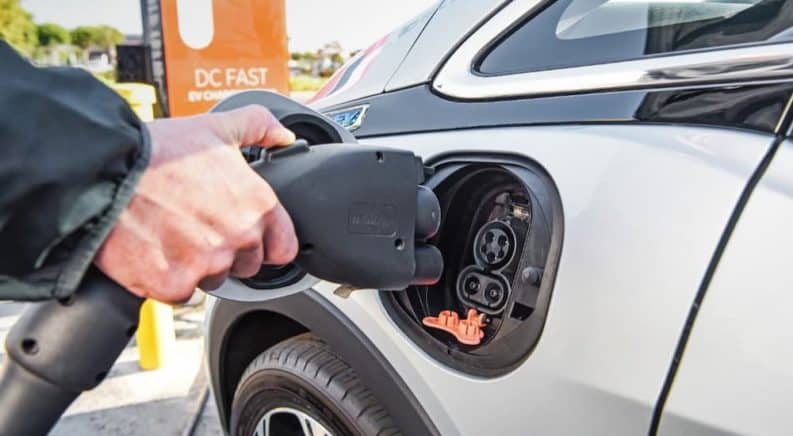 A closeup shows a charger being plugged into a silver 2020 Chevy Bolt EV.