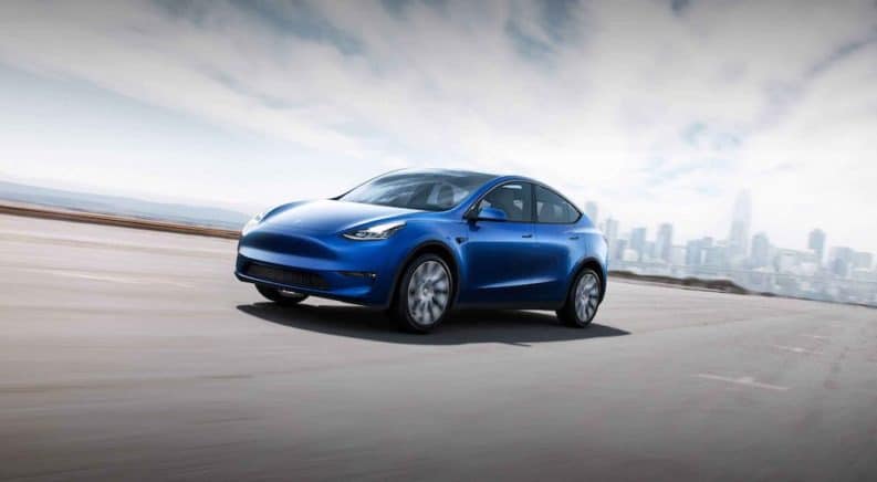 A common model in auto news, a blue 2021 Tesla Model Y, is driving on a highway away from a city.