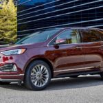 A dark red 2021 Ford Edge is parked in front of a glass building.