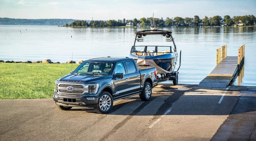 A blue 2021 Ford F-150 Limited is towing a boat out of a lake.