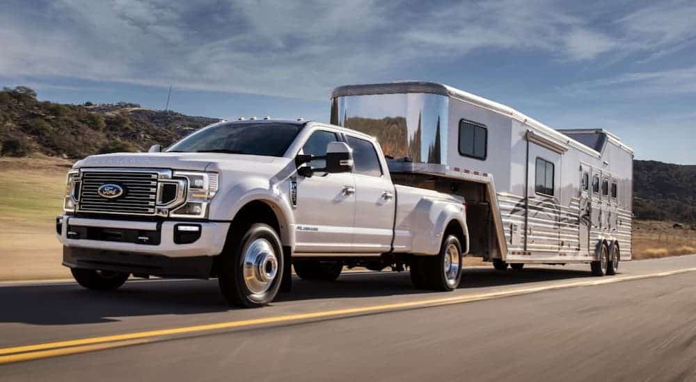 A popular Ford diesel truck, a white 2021 Ford F-450 diesel, is towing a large camper on a highway.