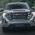 A grey 2021 GMC Sierra from a GMC dealer is driving on a winding road through pine trees.