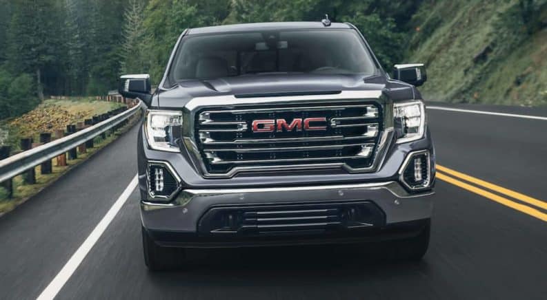 A grey 2021 GMC Sierra from a GMC dealer is driving on a winding road through pine trees.
