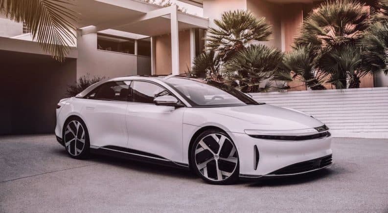 A white Lucid Motors Air is parked in front of a modern home with palm trees.