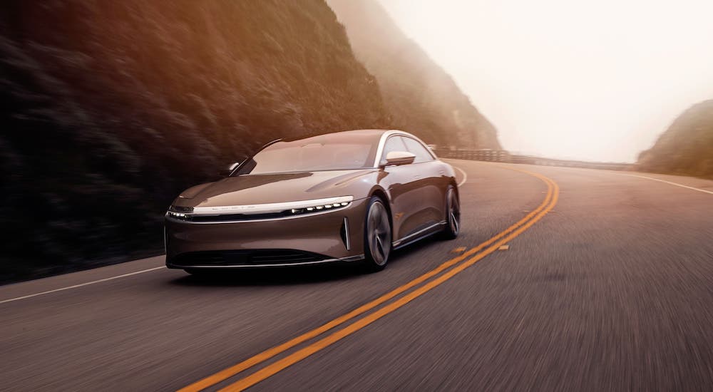 A gold Lucid Motors Air is driving around a mountain highway.