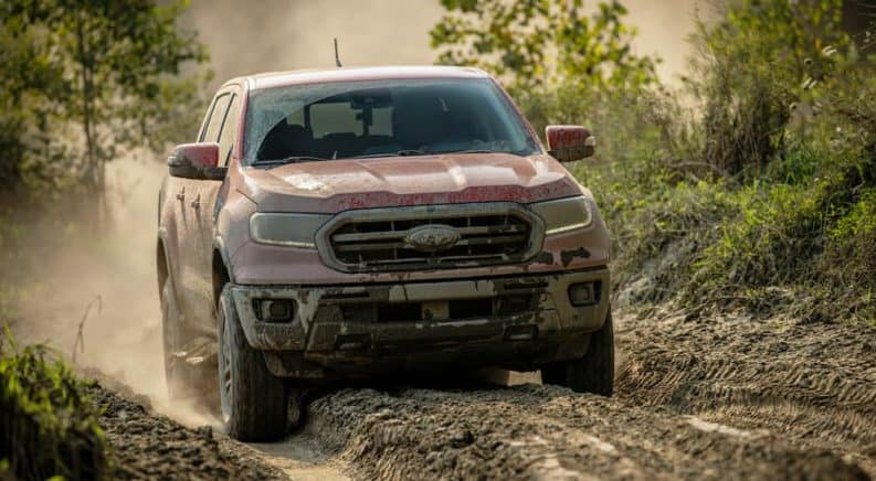 A red 2021 Ford Ranger Tremor Lariat is driving over a dirt path covered in mud.