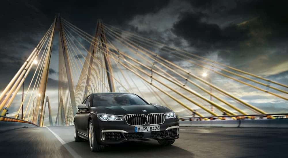 A black 2019 BMW M760i is driving over a cable bridge after leaving a used BMW dealer near you.