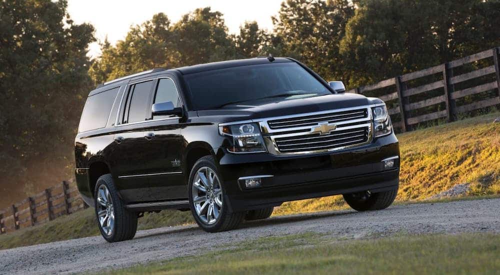 A black 2015 Used Chevy Suburban is parked on a gravel road in front of a fence.