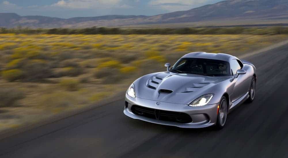 A silver 2015 Dodge Viper is driving on a road past a field and distant mountain.