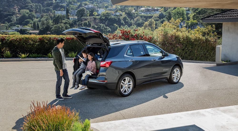 A man and children are sitting in the cargo area of a black 2021 Chevy Equinox that is parked in a driveway.