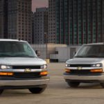 A white 2021 Chevy Express Cargo van and a silver Express Passenger van are parked on a city parking structure.