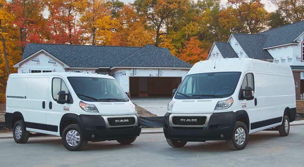 A white 2021 Ram ProMaster 3500 and ProMaster City are parked in front of a house under construction.