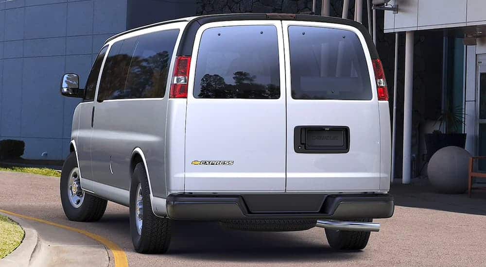 A silver 2021 Chevy Express is shown from the rear parked in front of a concrete building.
