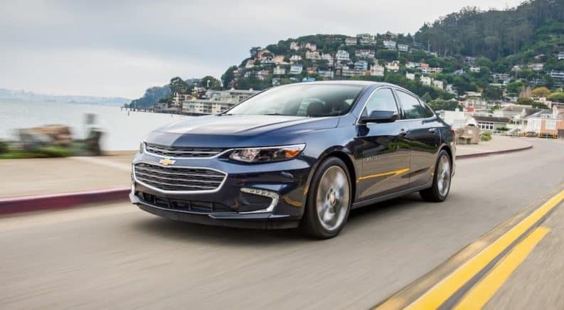 A blue 2021 Chevy Malibu is driving on a coastal highway.