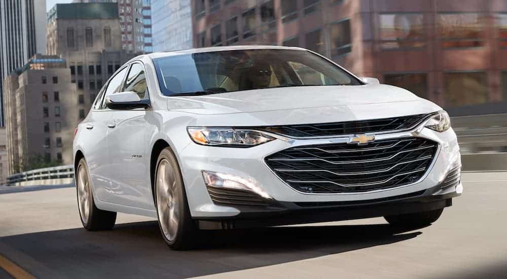 A white 2021 Chevy Malibu is driving on a city street.