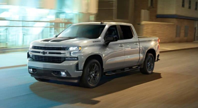 A silver 2021 Chevy Silverado 1500 is on a city street at night.