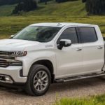 A white 2021 Chevy Silverado 1500 is driving on a dirt road past a field.