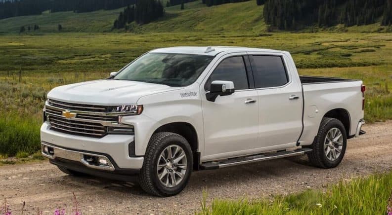 A white 2021 Chevy Silverado 1500 is driving on a dirt road past a field.