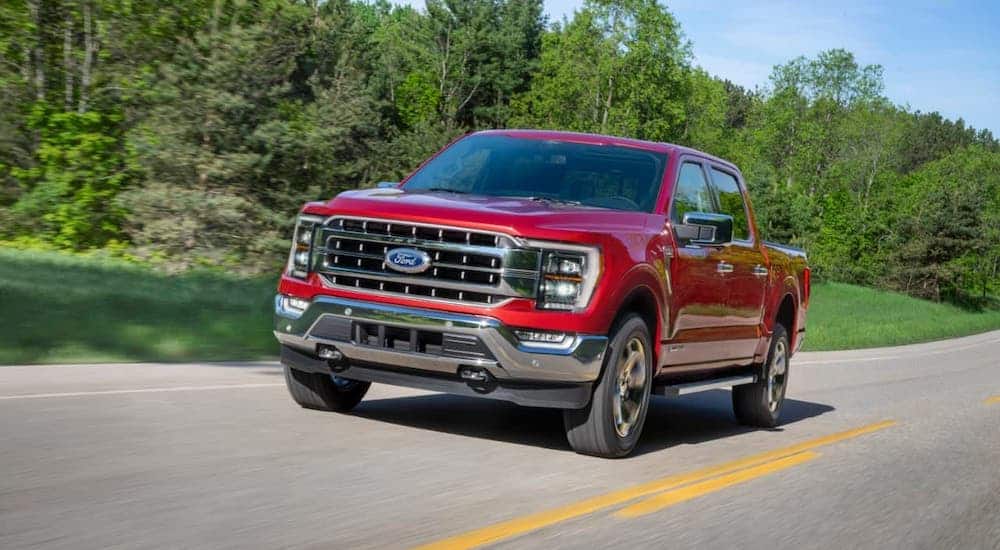 A red 2021 Ford F-150 is driving on a highway in front of trees.