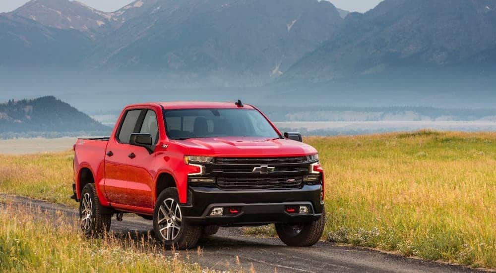 A red 2021 Chevy Silverado 1500 TrailBoss is driving on a dirt road in front of distant mountains.