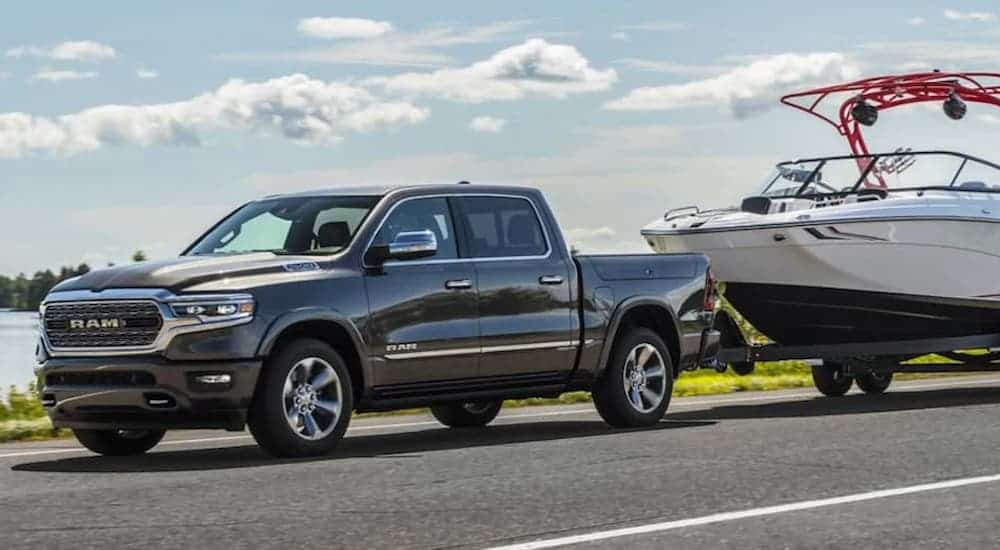 A grey 2021 Ram 1500 is towing a boat past water.