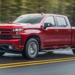 A red 2021 Chevy Silverado 1500 is driving past pine trees after winning the 2021 Chevy Silverado 1500 vs 2021 Ram 1500 comparison.