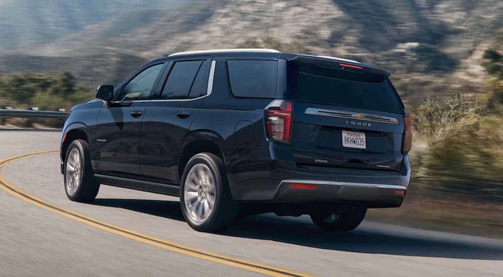 A black 2021 Chevy Tahoe is shown from the rear driving on a mountain road.