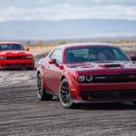 A red and an orange 2021 Dodge Challanger R/T Scat Pack Widebody are driving on a track covered in tire marks.