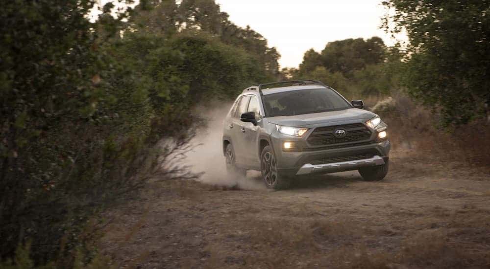 A gray 2021 Toyota RAV4 is driving on a dirt trail in the woods.