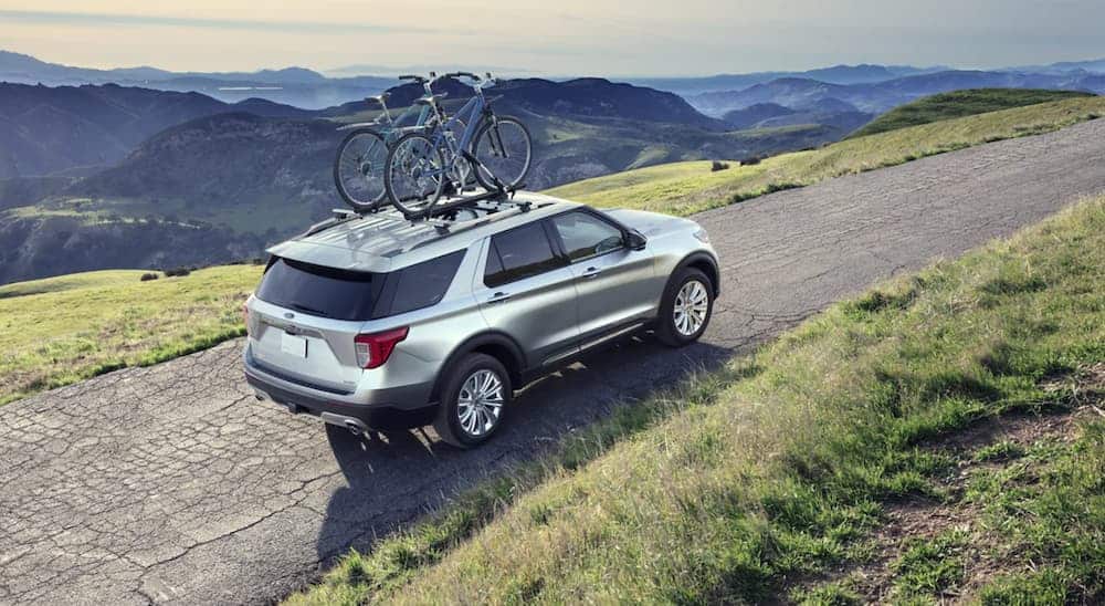 A silver 2021 Ford Explorer is driving on a narrow road with mountain views and bikes on the roof.