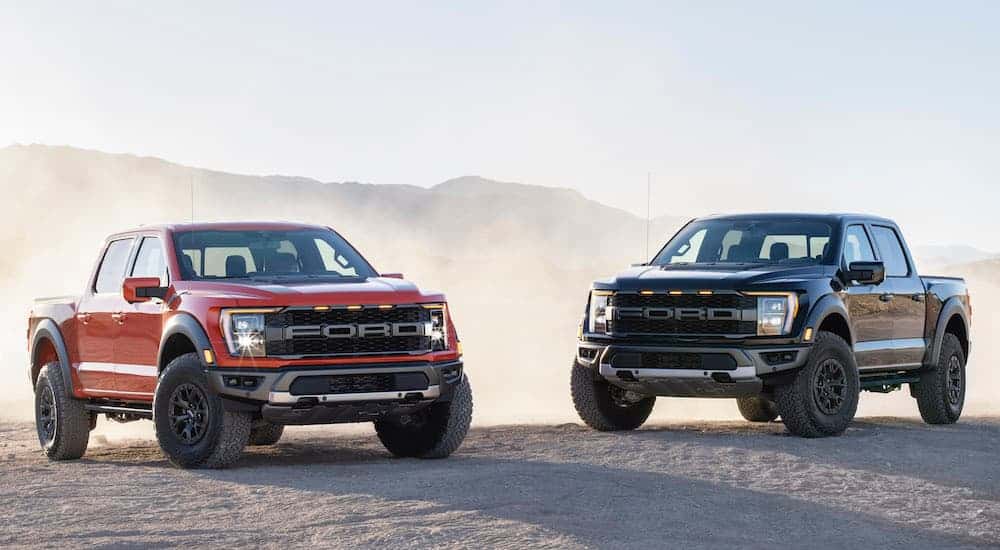 A black and a red 2021 Ford F-150 Raptor are parked in a dusty desert.