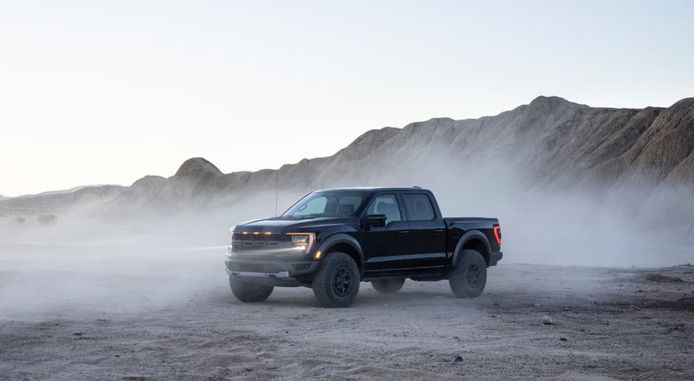 A black 2021 Ford F-150 Raptor is parked in front of a hill and a dusty desert.