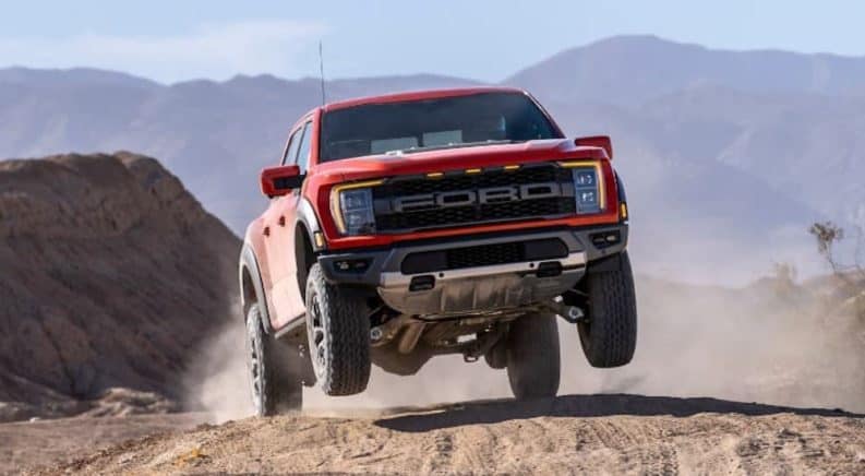 A red 2021 Ford F-150 Raptor is shown in the air after going over a dirt jump.