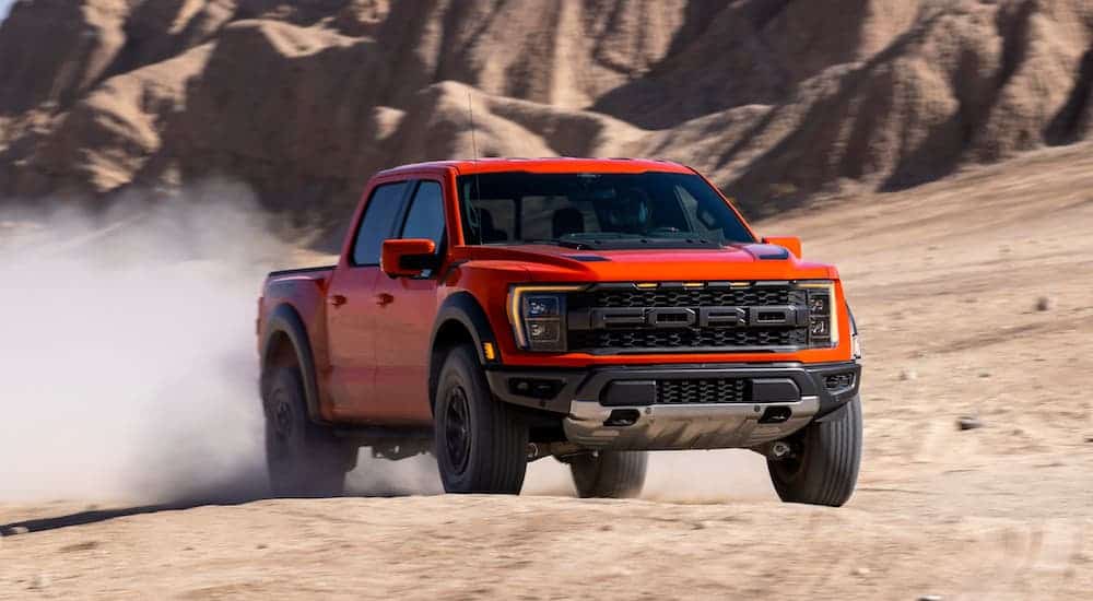 A red 2021 Ford F-150 Raptor is driving on sand in front of mountains.
