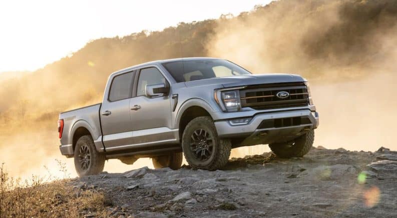 A silver 2021 Ford F-150 Tremor is off-roading in a dusty area at sunset.