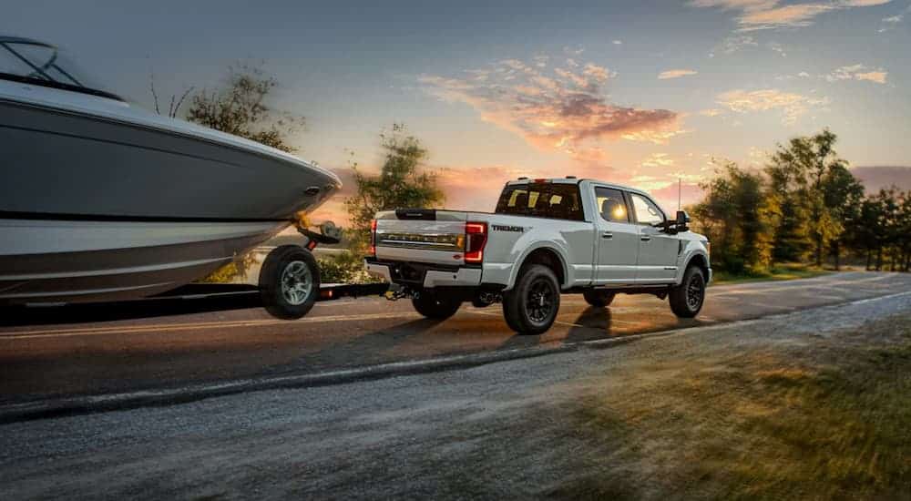 A white 2021 Ford F-250 Super Duty is towing a boat at sunset.