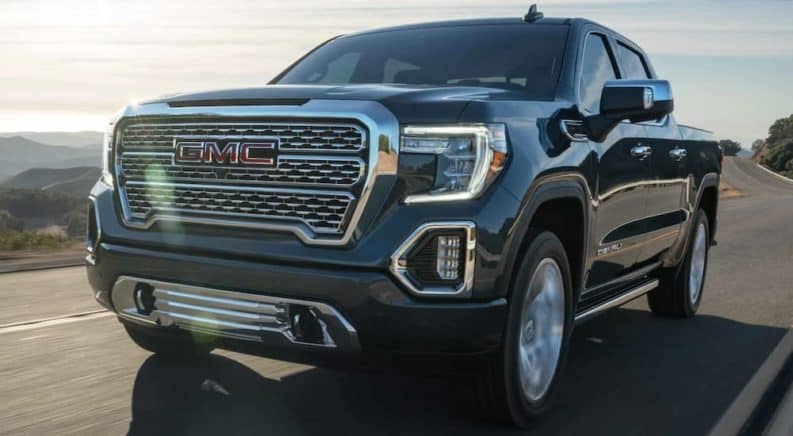 A grey 2021 GMC Sierra 1500 is driving on a road past mountains.