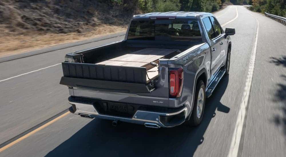 A grey 2021 GMC Sierra 1500 is shown from the rear driving with wood in the bed.