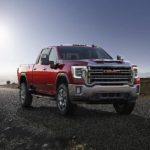 A red 2021 GMC Sierra 2500 HD SLT is on a highway against a bright blue sky.