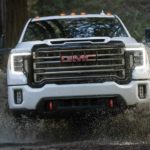 A white 2021 GMC Sierra 2500HD AT4 is shown from the front driving through a puddle in the woods.