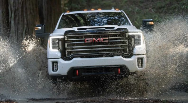 A white 2021 GMC Sierra 2500HD AT4 is shown from the front driving through a puddle in the woods.