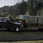 A black 2021 GMC Sierra 3500HD is towing a large gooseneck trailer up a hill.