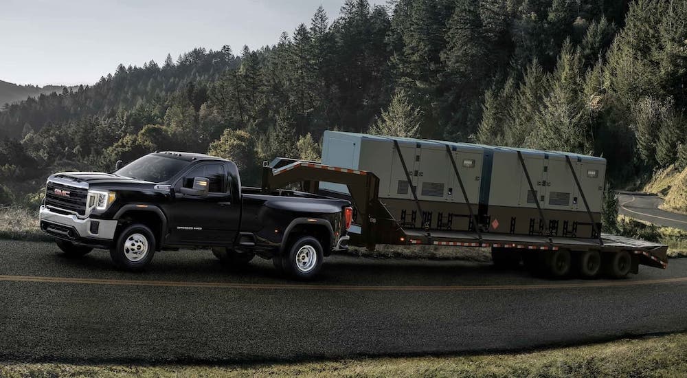 A black 2021 GMC Sierra 3500HD is towing a large gooseneck trailer up a hill.