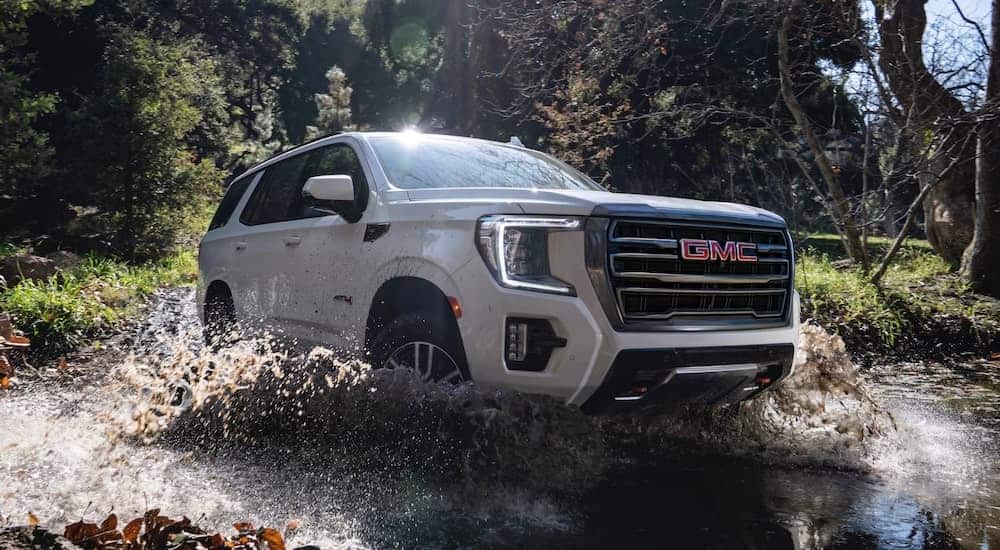 A white 2021 GMC Yukon AT4 is shown from the side splashing through a river.