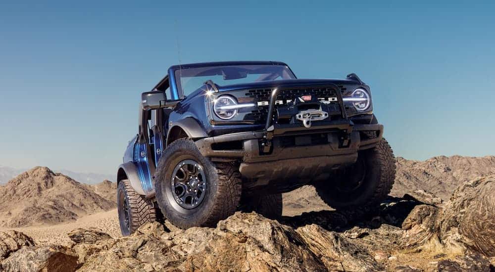 A blue 2021 Ford Bronco is parked while off-roading in the desert with no doors or roof.