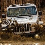 A white 2021 Jeep Wrangler Rubicon is off-roading in mud after winning the 2021 Jeep Wrangler vs 2021 Ford Bronco comparison.