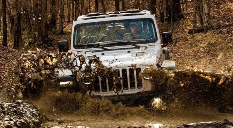 A white 2021 Jeep Wrangler Rubicon is off-roading in mud after winning the 2021 Jeep Wrangler vs 2021 Ford Bronco comparison.